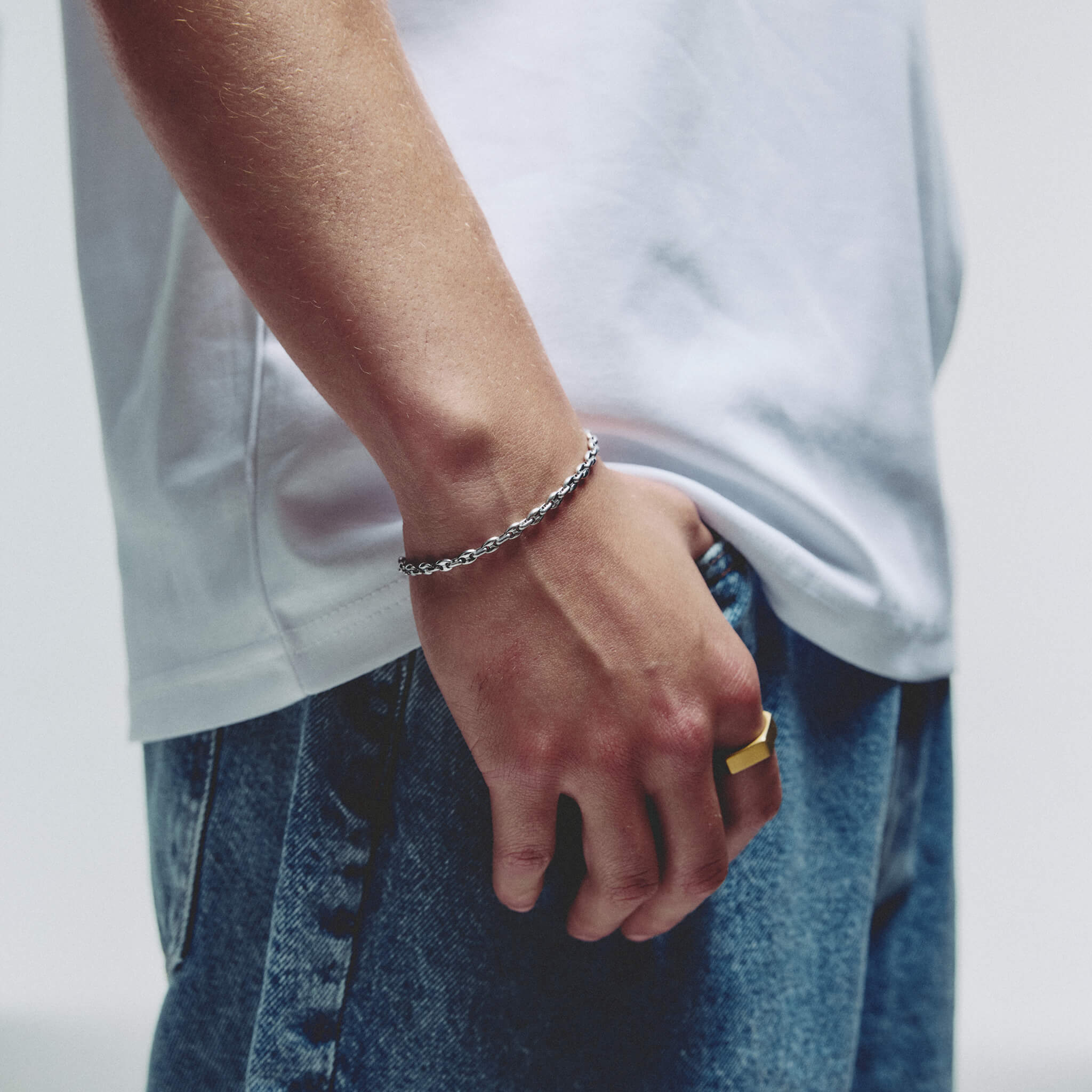 A close-up of a person wearing a silver mariner chain bracelet on their wrist, paired with a white t-shirt and blue jeans.