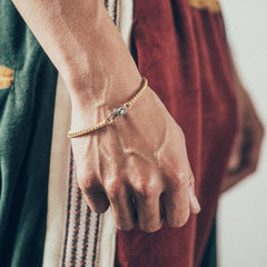 Close-up of wrist and hand featuring gold chain bracelet with silver oval clasp on textured fabric background
