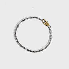 Silver chain bracelet with gold oval clasp on white background