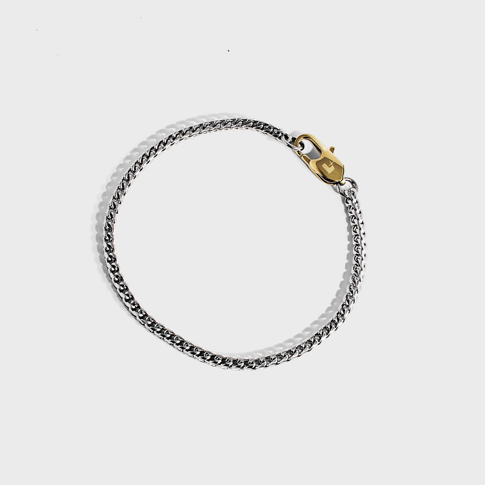 Silver chain bracelet with gold oval clasp on white background