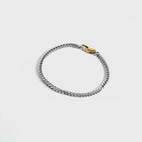 Silver chain bracelet with gold oval clasp on white background