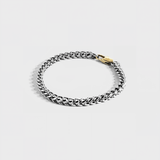 Silver chain bracelet with gold oval clasp on white background