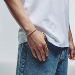 A close-up of a person wearing a delicate silver ball chain bracelet on their wrist, paired with a white t-shirt and blue jeans.