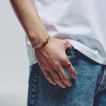 A close-up lifestyle shot of a person wearing a silver ball chain bracelet with gold geometric magnetic clasp on their wrist, paired with a white t-shirt and blue jeans.