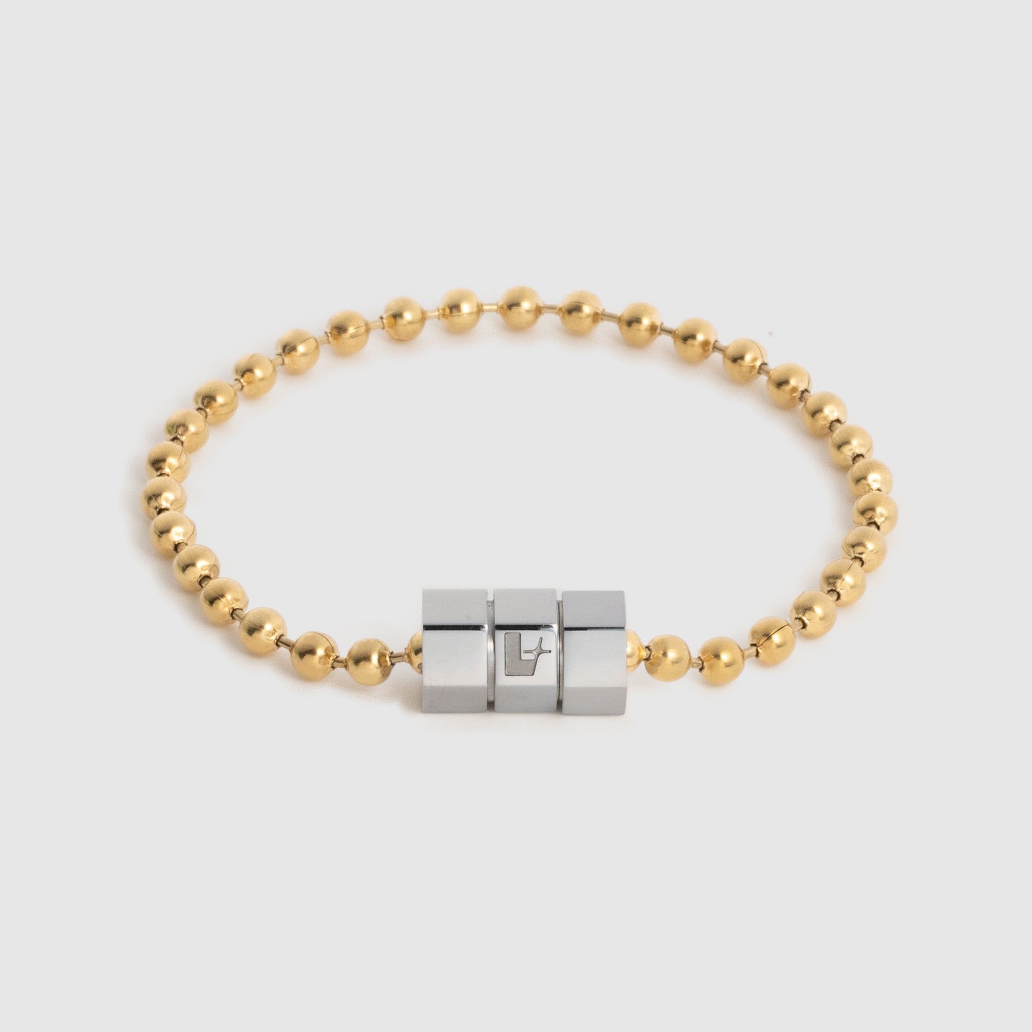 A gold ball chain bracelet with a central three-block hexagonal silver, magnetic clasp, photographed on a light gray background.