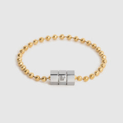 A gold ball chain bracelet with a central three-block hexagonal silver, magnetic clasp, photographed on a light gray background.