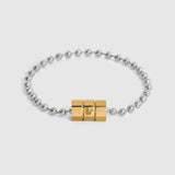 A silver beaded bracelet with a central gold hex shape magnetic clasp, featuring a small engraved 'L' logo, set against a light gray background.