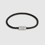 A black braided cord bracelet with a silver-toned hex block magnetic clasp featuring an engraved "L", shown on a light gray background.