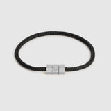 A black braided cord bracelet with a silver-toned hex block magnetic clasp featuring an engraved "L", shown on a light gray background.