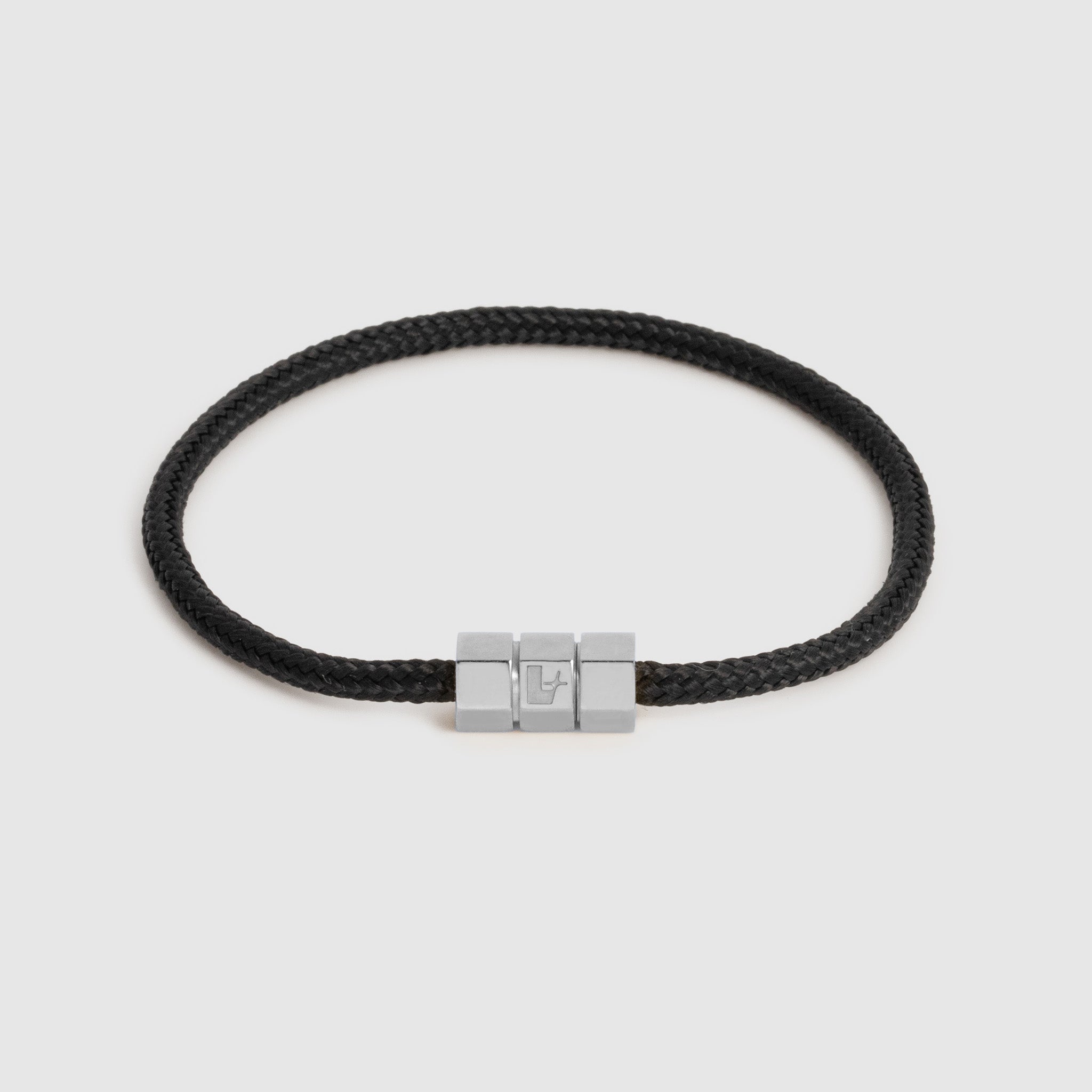 A black braided cord bracelet with a silver-toned hex block magnetic clasp featuring an engraved "L", shown on a light gray background.