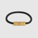 A black braided cord bracelet with a gold- hex block magnetic clasp, shown on a light gray background.