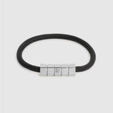 A black cord bracelet with a polished silver-toned geometric block clasp, shown on a light gray background.