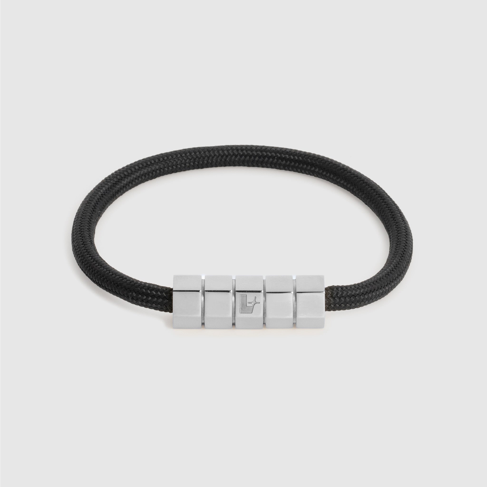 A black cord bracelet with a polished silver-toned geometric block clasp, shown on a light gray background.
