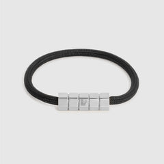 A black cord bracelet with a polished silver-toned geometric block clasp, shown on a light gray background.