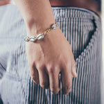 Close-up of wrist wearing silver mariner-link bracelet with gold oval clasp on textured fabric background