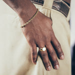 Close-up of hand and wrist wearing gold mariner chain bracelet and gold signet ring on textured background