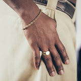 Close-up of hand and wrist wearing gold mariner chain bracelet and gold signet ring on textured background