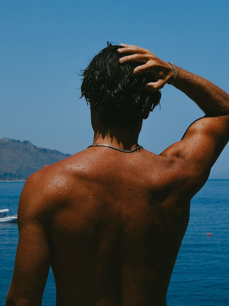 Man looking out at water wearing cuban chain necklace and bracelet.