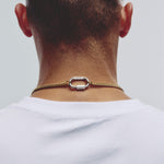 A close-up back view of a man's neck and upper shoulders, wearing a gold chain necklace with a textured silver-toned oval clasp over a white t-shirt.
