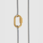 A close-up of a necklace featuring a gold carabiner clasp hanging from a two-tone chain with silver and gold links, set against a light gray background.