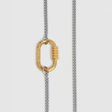 A close-up of a necklace featuring a gold carabiner clasp hanging from a two-tone chain with silver and gold links, set against a light gray background.