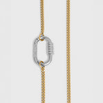 A close-up of a gold-toned chain necklace with a silver-toned carabiner clasp, shown against a light gray background.