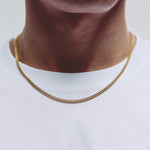 A close-up of a person's neck and upper chest wearing a gold chain necklace over a white t-shirt.