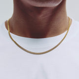 A close-up of a person's neck and upper chest wearing a gold chain necklace over a white t-shirt.