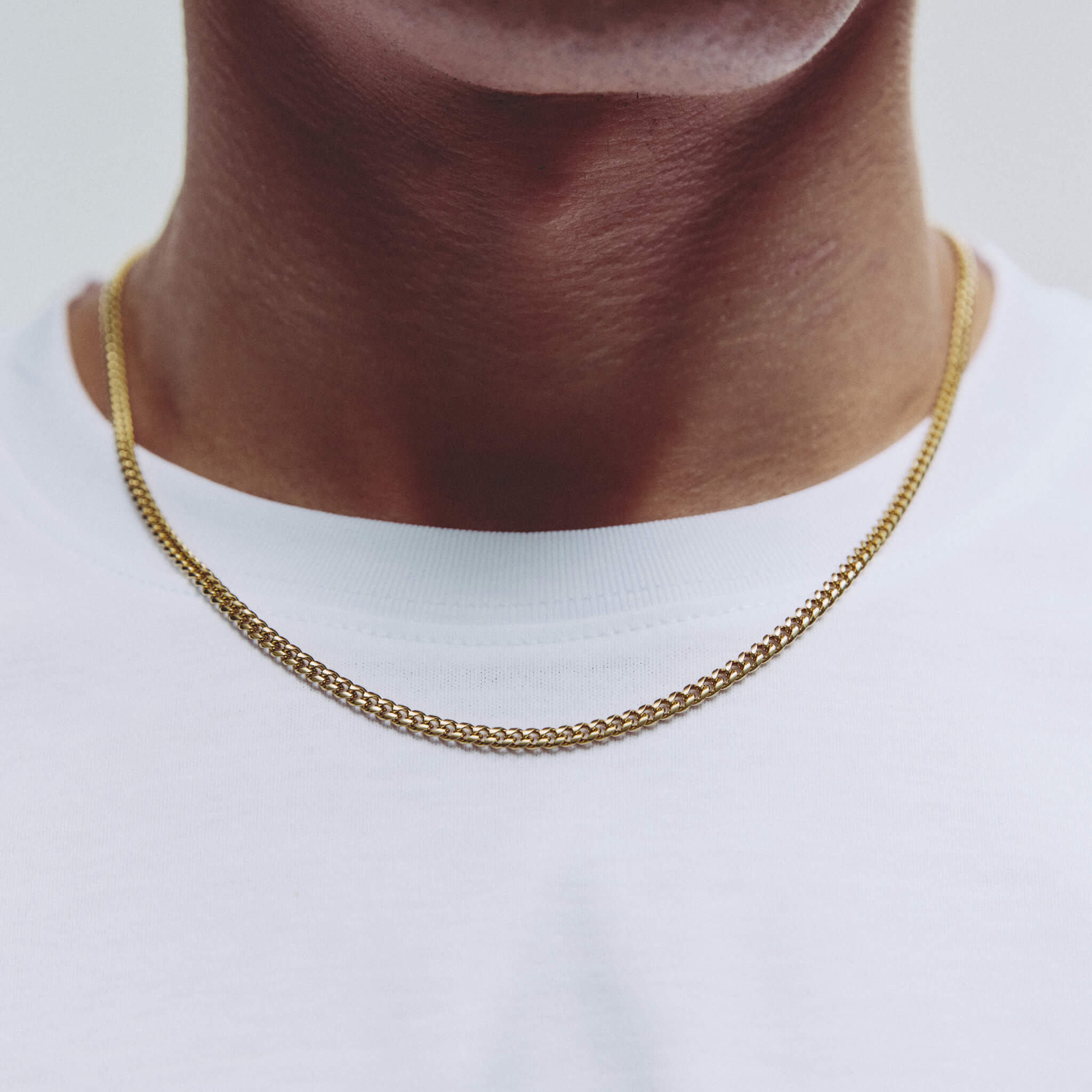 A close-up of a person's neck and upper chest wearing a gold chain necklace over a white t-shirt.