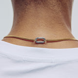 A close-up of a person's neck and upper chest wearing a delicate gold chain necklace with a central silver-toned carabiner clasp paired with a white t-shirt.