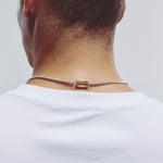 A close-up back view of a man wearing a silver chain necklace with a gold oval clasp, paired with a white t-shirt against a light gray background.