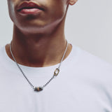 A close-up of a man wearing a silver ball-chain necklace with a gold carabiner clasp and small hexagonal pendant beads, paired with a white t-shirt.