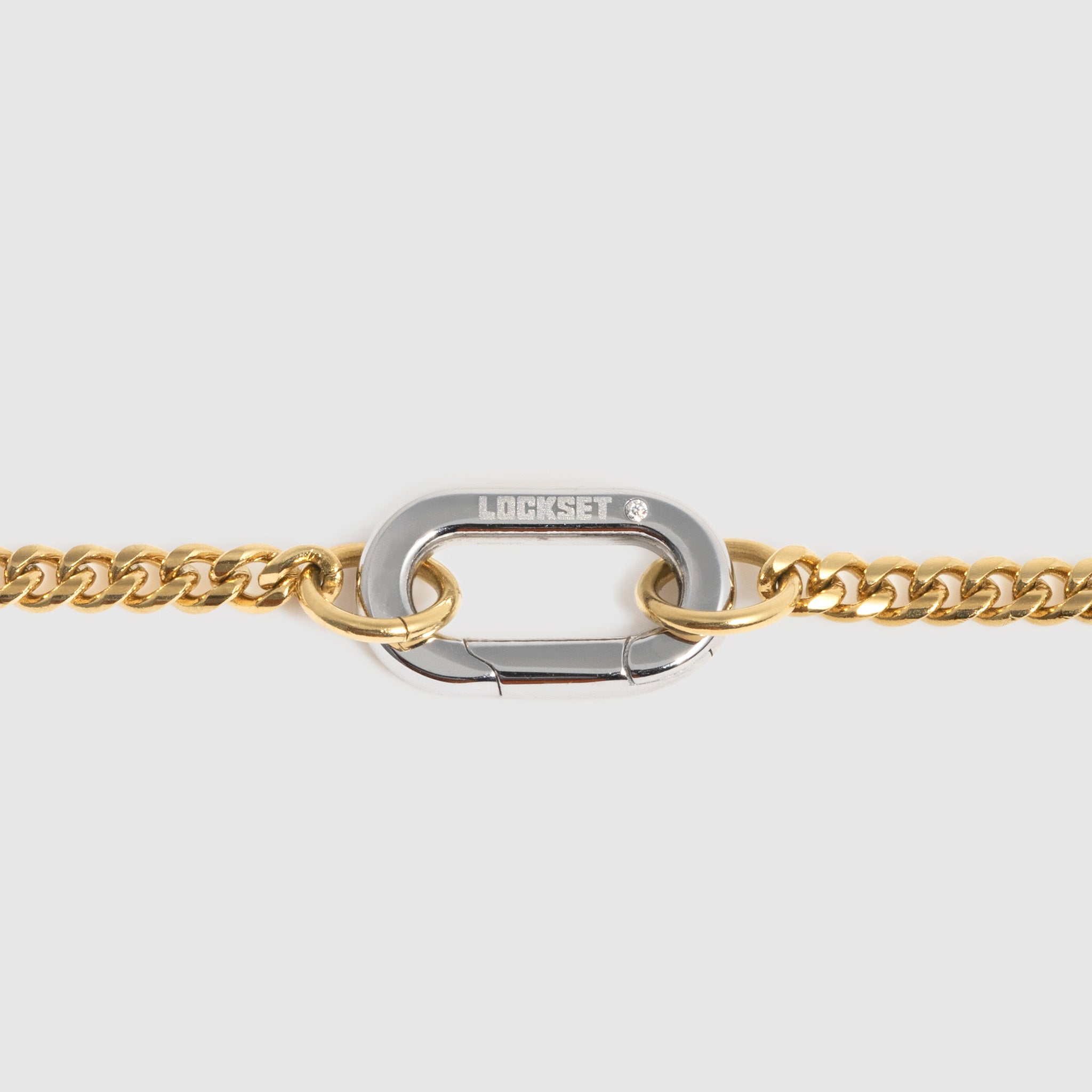 A close-up of a gold chain bracelet featuring a central silver-toned carabiner clasp engraved with the brand name Lockset