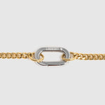 A close-up of a gold chain featuring a central silver-toned carabiner clasp engraved with the brand name 'Lockset". 
