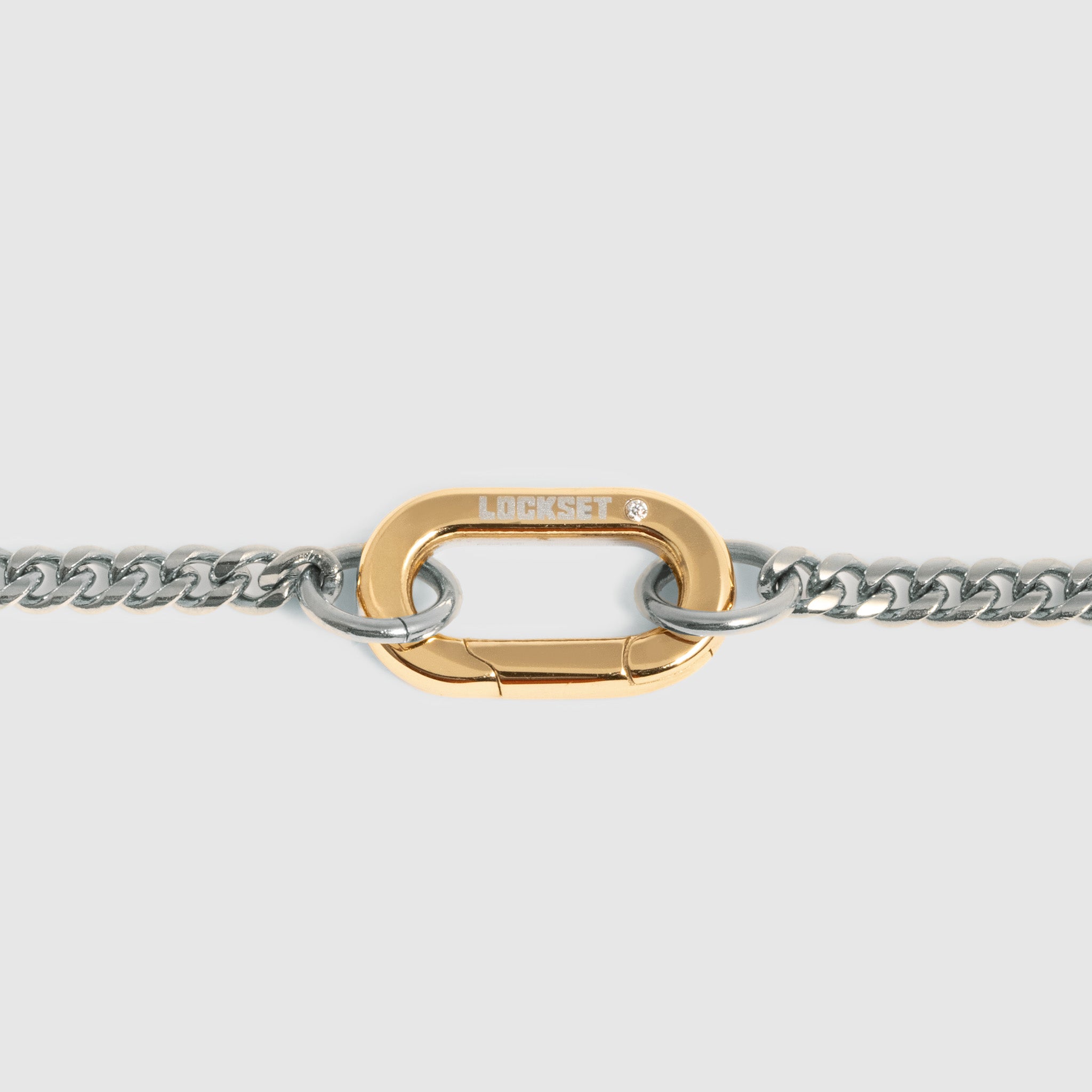 A close-up of a gold carabiner clasp connected to a silver-tone curb chain, shown against a light gray background.