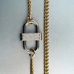 Gold chain necklace with silver double-lock pendant featuring centered diamond detail on gray background”