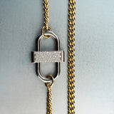 Gold chain necklace with silver double-lock pendant featuring centered diamond detail on gray background”