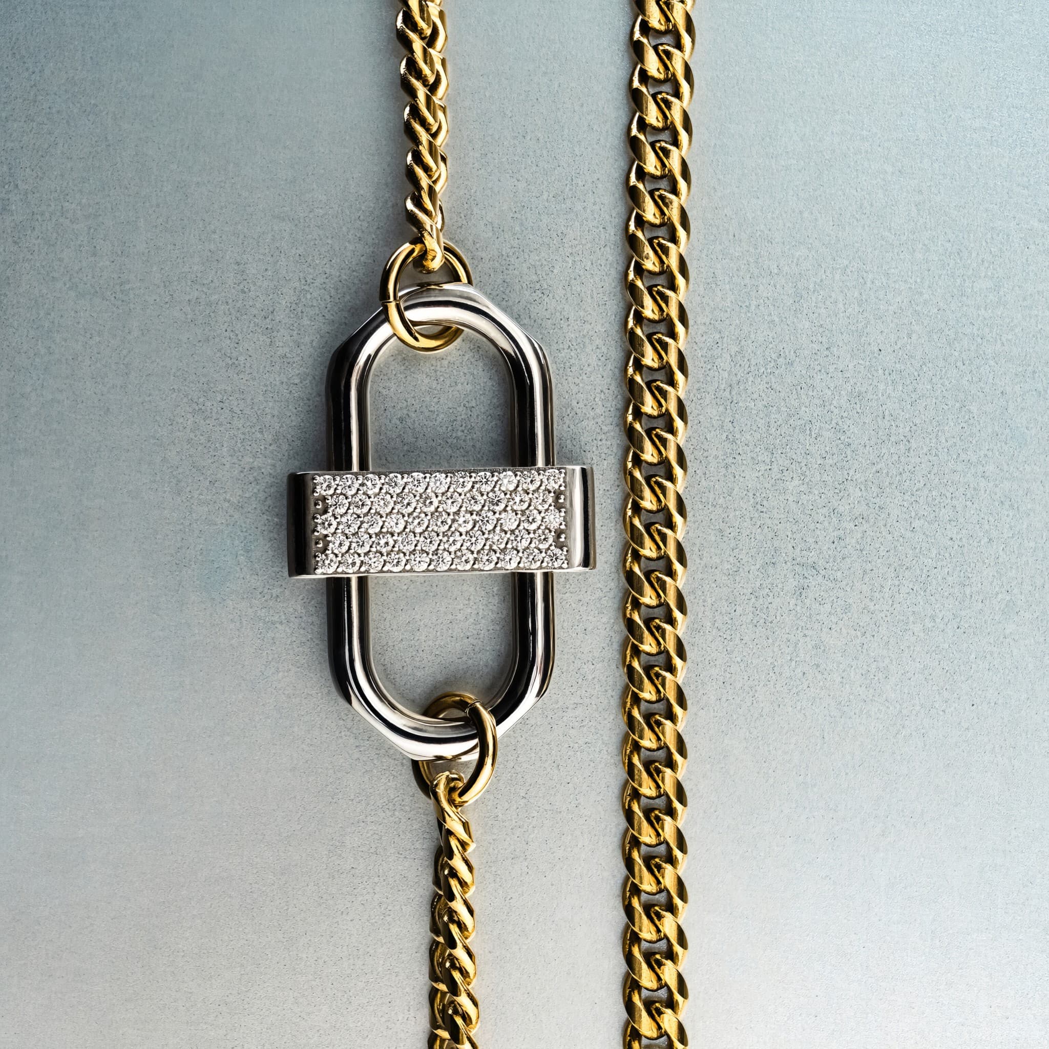 Gold chain necklace with silver double-lock pendant featuring centered diamond detail on gray background”