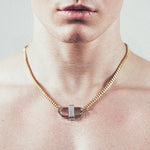 Close-up of man wearing gold chain necklace with silver double-lock pendant featuring centered diamond detail