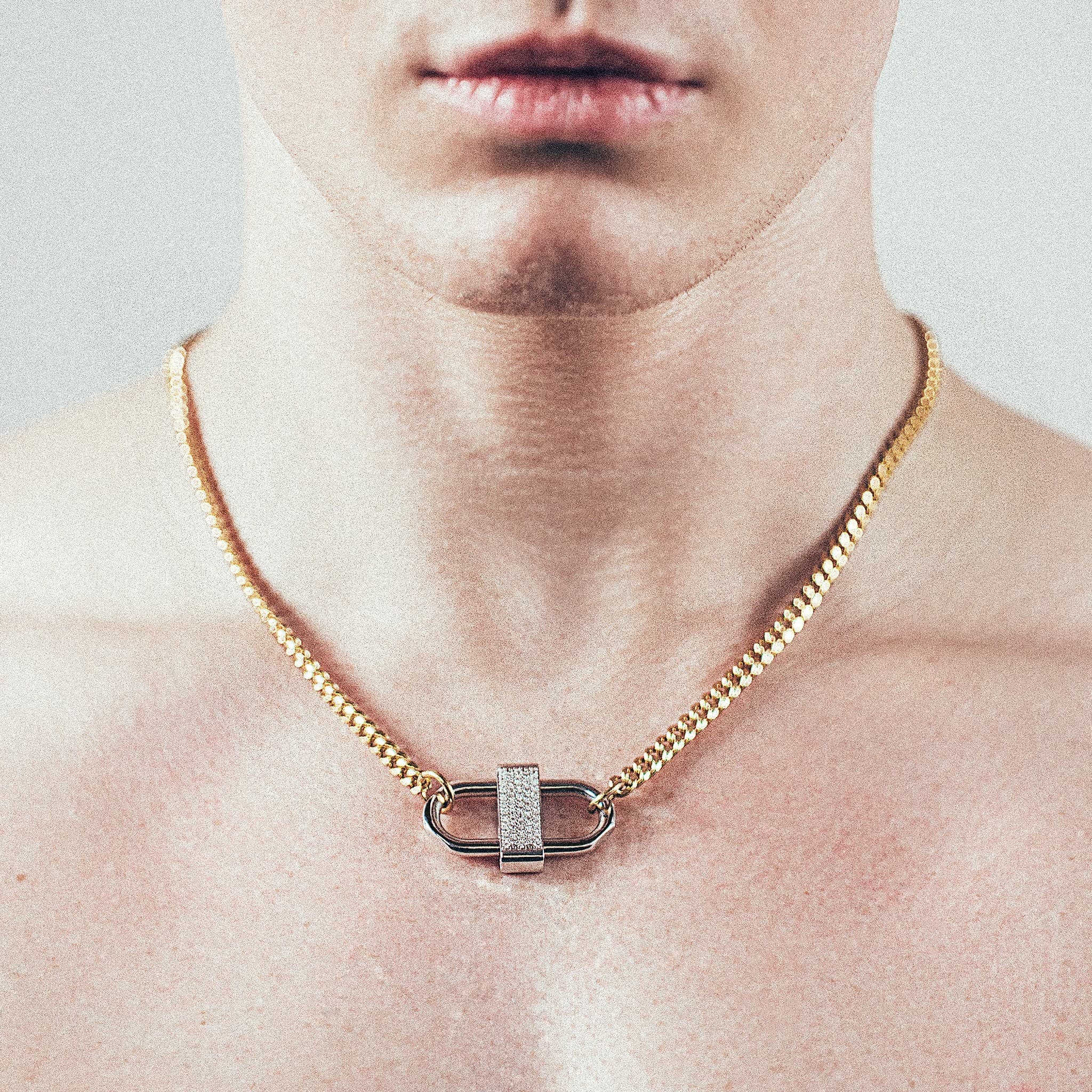Close-up of man wearing gold chain necklace with silver double-lock pendant featuring centered diamond detail