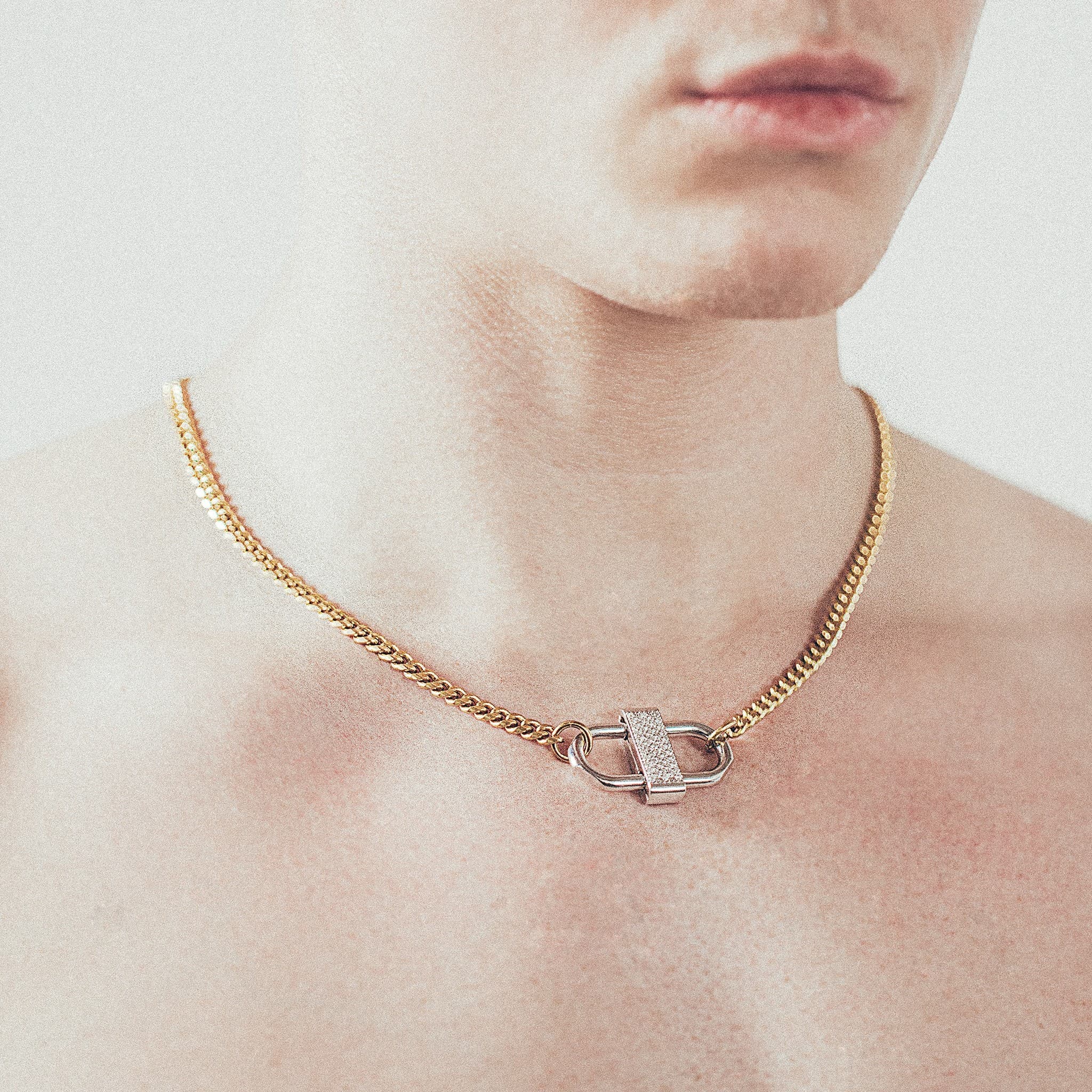 Close-up of man wearing gold chain necklace with silver double-lock pendant featuring centered diamond detail