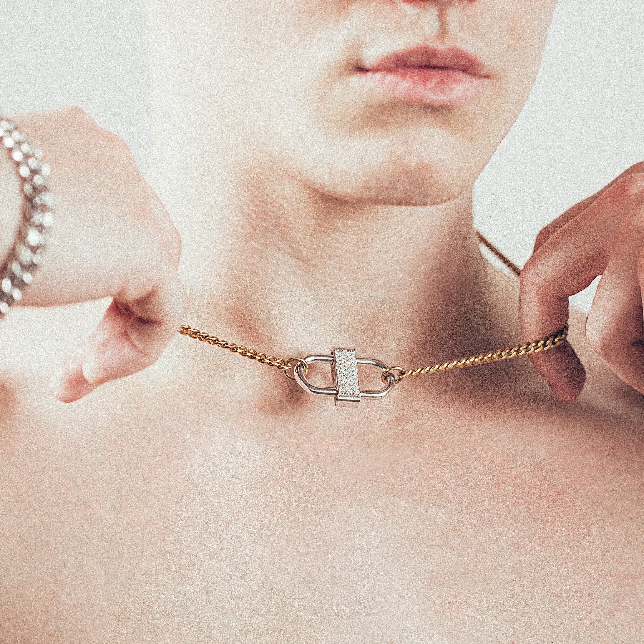Close-up of man wearing gold chain necklace with silver double-lock pendant featuring centered diamond detail