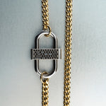 Gold chain necklace with silver double-lock pendant featuring centered black diamond detail on gray background