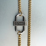 Gold chain necklace with silver double-lock pendant featuring centered black diamond detail on gray background