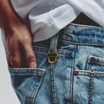 Close-up of a person wearing blue denim jeans with a gold and green enamel lock accessory attached to belt loop and silver chain.  