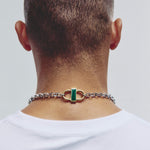A close-up back view of a man wearing a silver chain necklace with a distinctive gold and green clasp at the base of his neck.