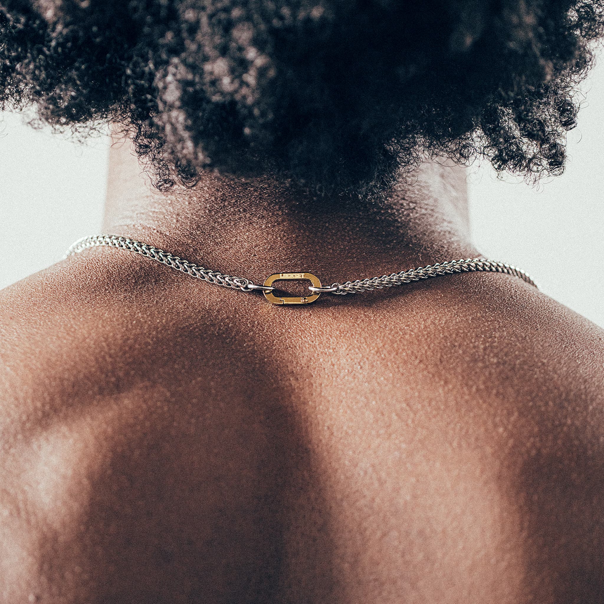 Close-up of man wearing silver chain necklace with gold carabiner clasp