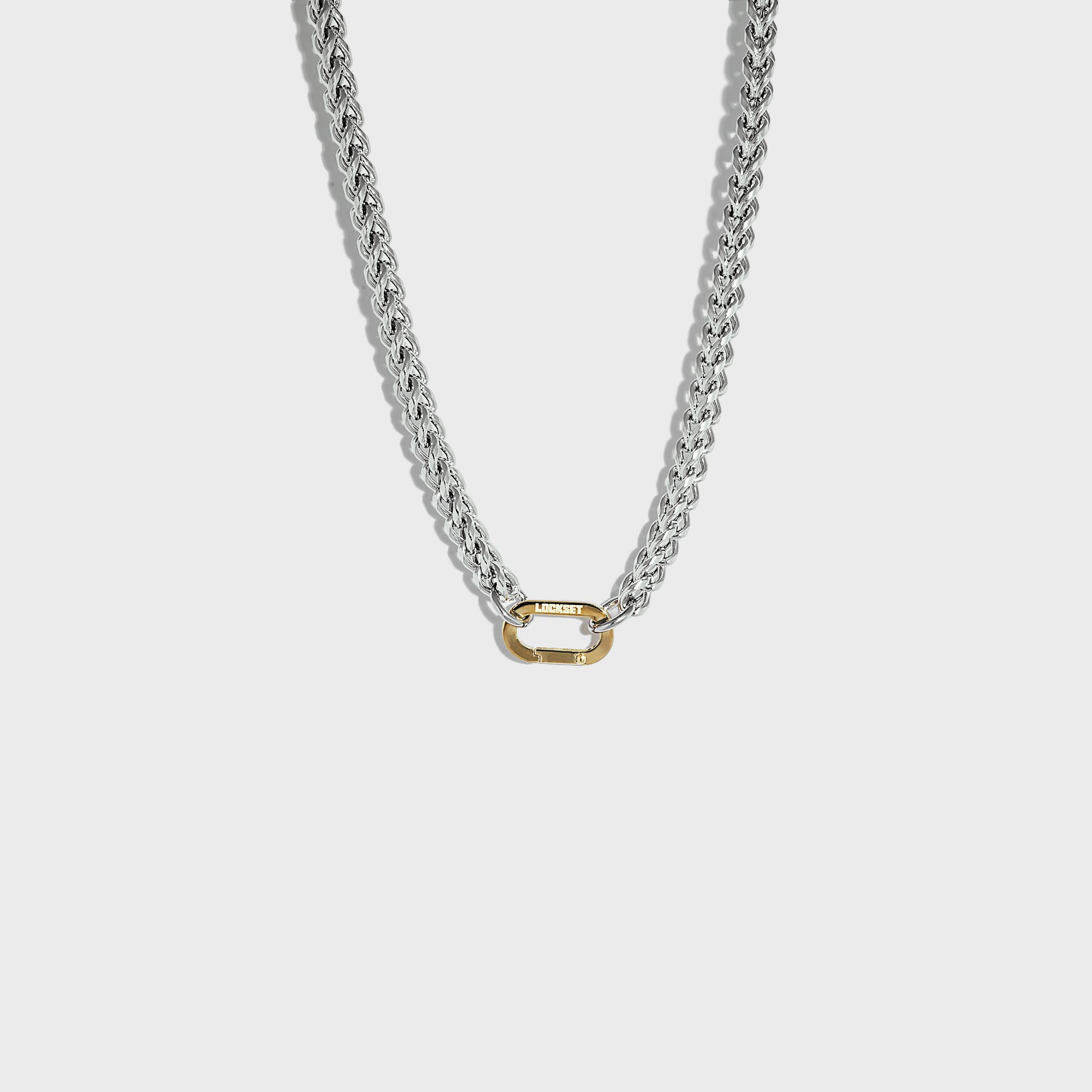 Thick silver chain necklace with gold carabiner clasp on white background