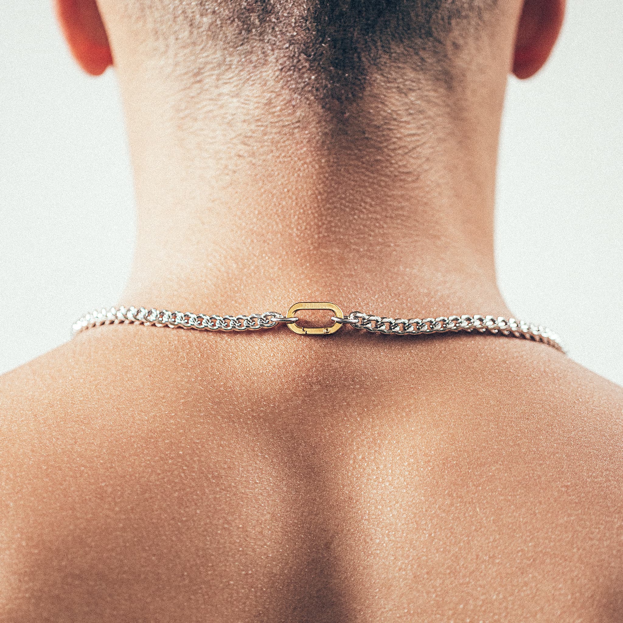 Close-up of man wearing silver chain necklace with gold carabiner clasp 