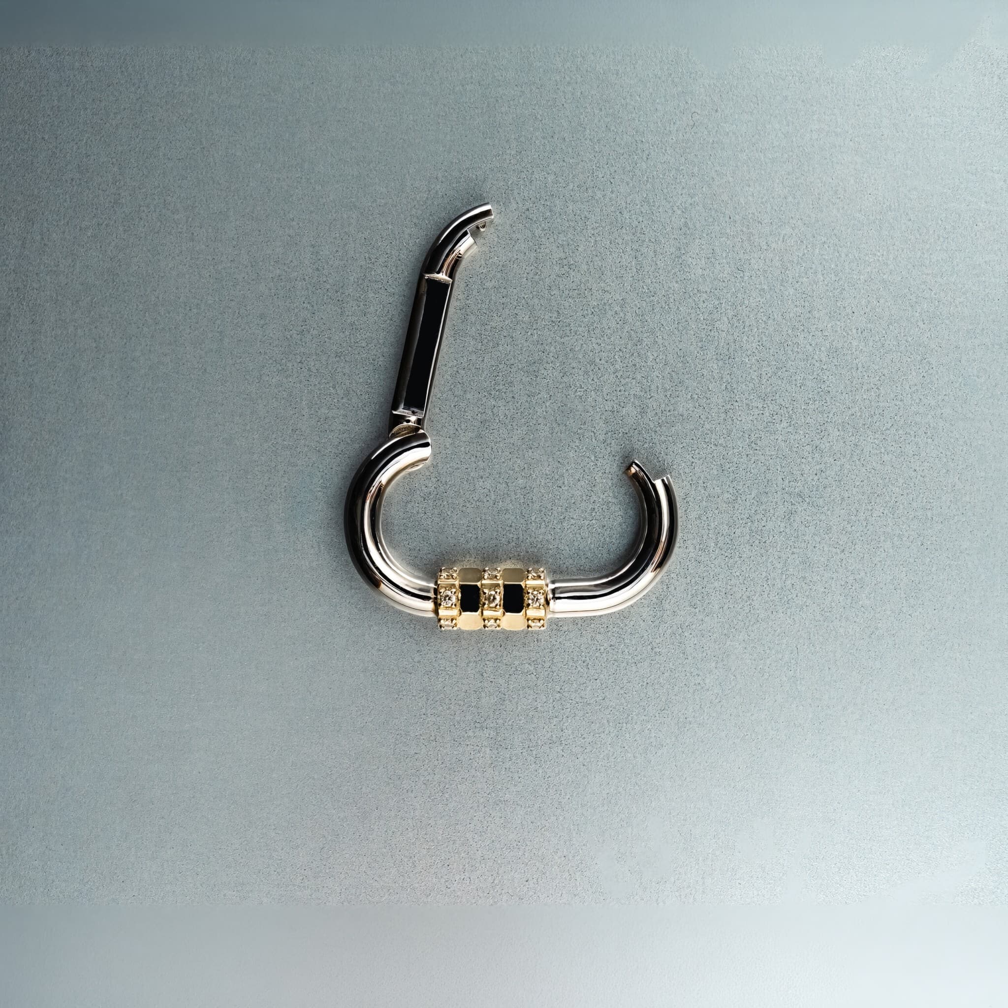Open silver carabiner pendant featuring gold lock with diamond details on gray background